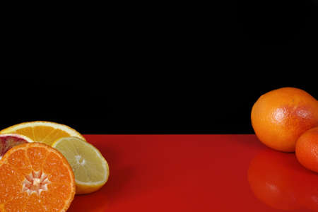 Various fresh citrus fruits, orange, blood orange, mandarin, lemon on red table top and black background, copy spaceの写真素材