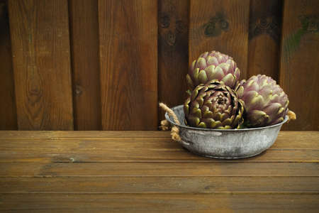 Fresh big Romanesco artichokes green-purple flower heads in tin bowl on wooden backgroundの写真素材