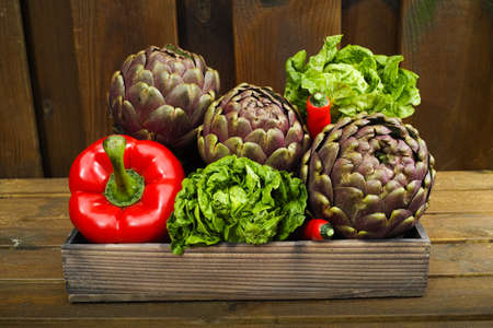 Fresh big Romanesco artichokes green-purple flower heads, red paprika, romanine lettuce on wooden backgroundの写真素材