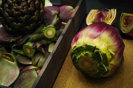 Fresh artichoke green-purple flower head on cutting board with knifeの写真素材