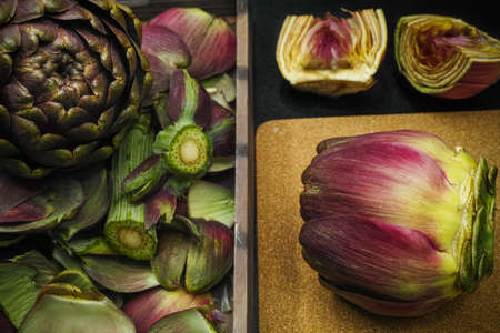 Fresh artichoke green-purple flower head on cutting board with knifeの写真素材