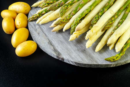 Organic fresh white and green asparagus and potatoes on black background, rustic style, copy spaceの写真素材