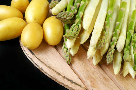 Organic fresh green and white asparagus and potatoes on wooden table and black backgroundの写真素材