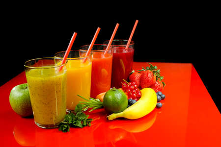Colorful fresh pressed fruit green, yellow, oragne and red juices with fresh fruits and berries on black and red backgroundの写真素材