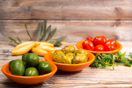 Tapas orange bowls  with giant  green olives and cherry tomatoes on wooden background, copy spaceの写真素材