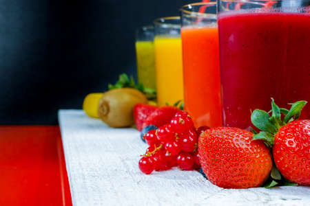 Colorful fresh pressed fruit green, yellow, oragne and red juices with fresh fruits and berries on black and red backgroundの写真素材