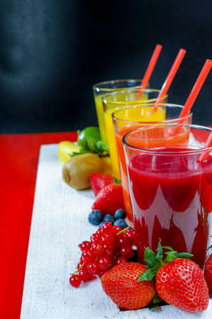 Colorful fresh pressed fruit green, yellow, oragne and red juices with fresh fruits and berries on black and red backgroundの写真素材