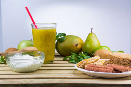 Green fruits and vegetables, fresh pressed smoothie in tall glass and yougurt on wooden background, breakfast conceptの写真素材