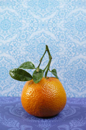 Fresh mandarin oranges fruit with green leaves on blue-purple backgroundの写真素材