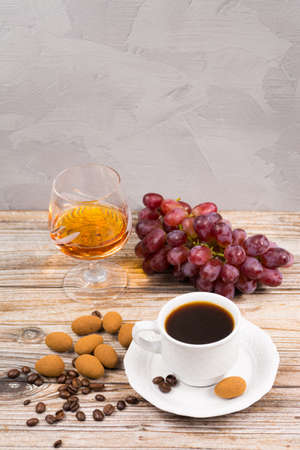 Amber color brandy with cup espresso,  green and red fresh grape and chocolate eggs on wooden backdroundの写真素材