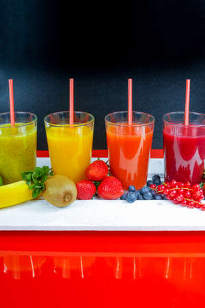 Colorful fresh pressed fruit green, yellow, oragne and red juices with fresh fruits and berries on black and red backgroundの写真素材