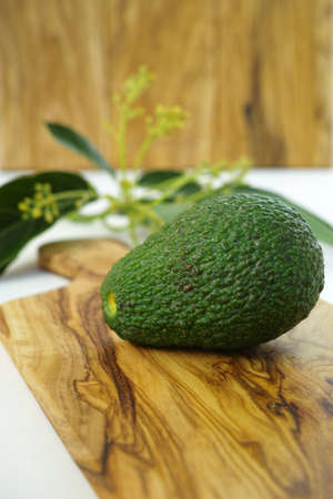 Fresh green avocados with leaves on olive wood cutting board