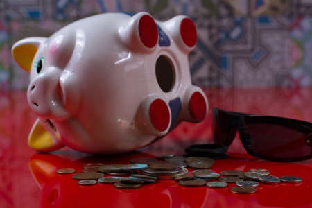 Opened piggy bank with black sunglasses and rolls cash on red backgroundの写真素材