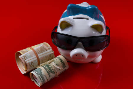Piggy bank with black sunglasses and rolls cash on red backgroundの写真素材