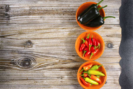 Mexican hot chili peppers colorful mix jalapeno on orange bowls and wooden black backgroundの写真素材