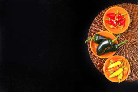 Mexican hot chili peppers colorful mix jalapeno on orange bowls and black background