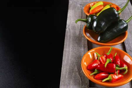 Mexican hot chili peppers colorful mix jalapeno on orange bowls and black backgroundの写真素材