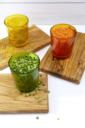 Multicolored clear glasses with various legumes ( green peas, red lentils, yellow indian lentils) on...