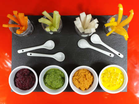Healthy snacks - colofrul vegetable sticks and mousses on red and black background
