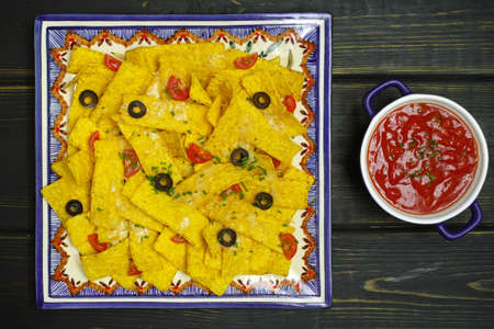 A plate of delicious tortilla nachos with melted cheese sauce, chives onion, black olives, salsa on...