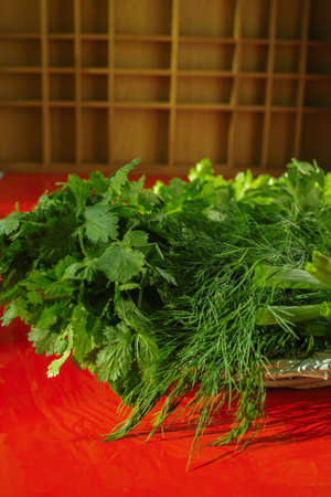 Fresh green herbs in the wicker basket - parsley, coriander, green onion, dill on red backgroundの写真素材
