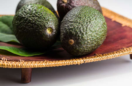Green fresh avocado with leaves on wooden background