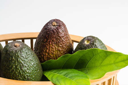 Green fresh avocado with leaves on wooden background