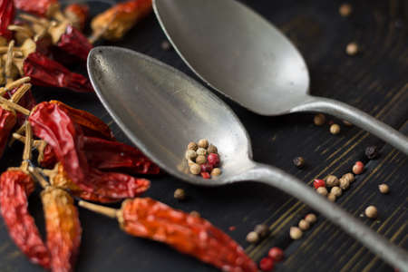Two old tin spoons with red hot chili cayenne peppers dried, variety - spicy ingredient on wooden tableの写真素材