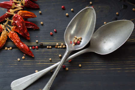 Two old tin spoons with red hot chili cayenne peppers dried, variety - spicy ingredient on wooden tableの写真素材