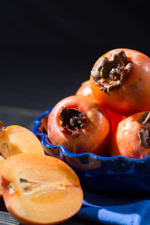 Ripe orange hachiya persimmons in blue bowl