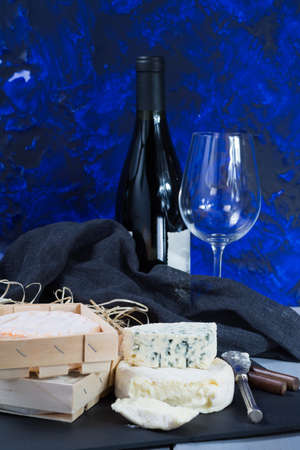 French soft cheeses on black stone platter and bottle with red wineの写真素材
