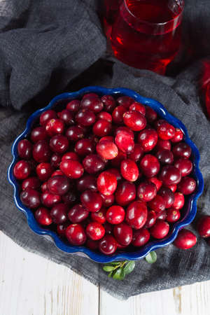 Red cranberry juice in a glass, cranberries in the blue clay bowl on the table, blue wall