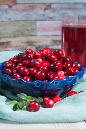Red cranberry juice in a glass, cranberries in the blue clay bowl on the table, blue wallの写真素材