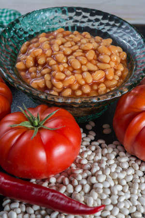 Traditional English food - baked white beans in tomato sauce and ingredients ready to cook - tomatoes, dried white beans and onionの写真素材