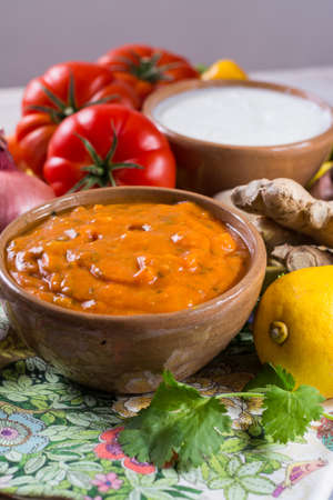 Bowl of vegetable Tikka Masala sauce and ingredients that go into making it - red tomatoes, chili pepper, carrot, coriander leaves, onion, garlic, gember. Used widely in Indian food.の写真素材