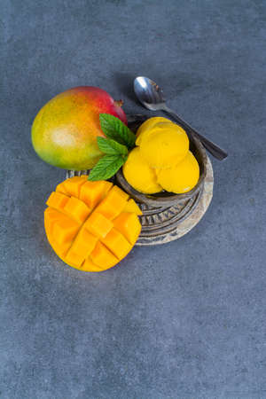 Mango ice cream sorbet with mint leaves and mango fruit in black stone bowlの写真素材