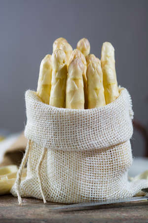 Spring season - fresh white big asparagus in burlap sack on granite plank backgroundの写真素材