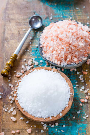 Different types of natural salt in stone bowls on wooden surface. White sea salt, pink Himalayan saltの写真素材