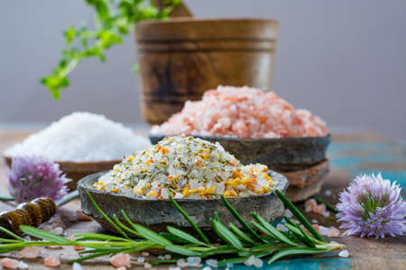 Different types of natural salt in stone bowls on wooden surface. White sea salt, pink Himalayan salt, Spiced salt with rosemaryの写真素材
