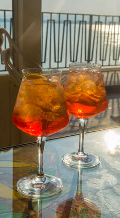 Waiter prepared the Aperol Sprits summer cocktail with Aperol, prosecco, ice cubes and orange in wine glass, ready to drink on sunny terrace with sea viewの写真素材