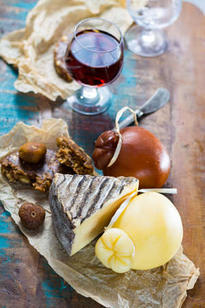 Sweet dessert liqueur wine in glass, hard cheeses Caciocavallo or Provolone, Tomme de Montagne, dried figs with figs bread, still life on wooden platterの写真素材