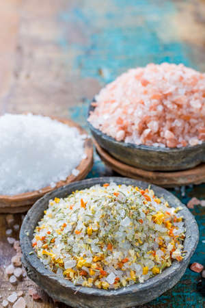 Different types of natural salt in stone bowls on wooden surface. White sea salt, pink Himalayan salt, Spiced salt with rosemaryの写真素材