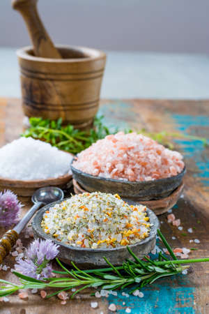 Different types of natural salt in stone bowls on wooden surface. White sea salt, pink Himalayan salt, Spiced salt with rosemaryの写真素材