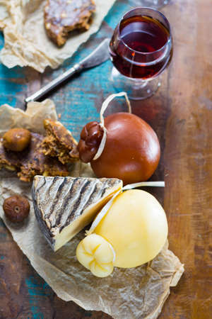 Sweet dessert liqueur wine in glass, hard cheeses Caciocavallo or Provolone, Tomme de Montagne, dried figs with figs bread, still life on wooden platterの写真素材