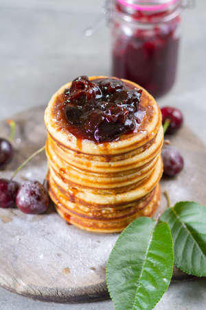 Homemade American pancakes served with cherry jam and fresh cherry on a wooden background, sweet dessertの写真素材