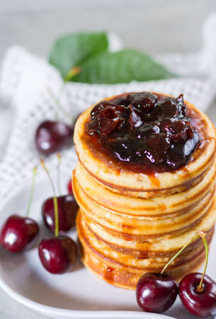 Homemade American pancakes served with cherry jam and fresh cherry on a wooden background, sweet dessertの写真素材