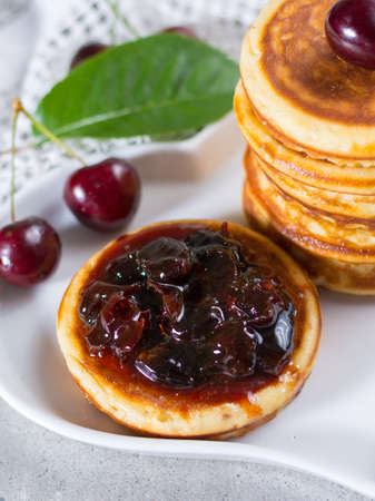 Homemade American pancakes served with cherry jam and fresh cherry on a wooden background, sweet dessertの写真素材
