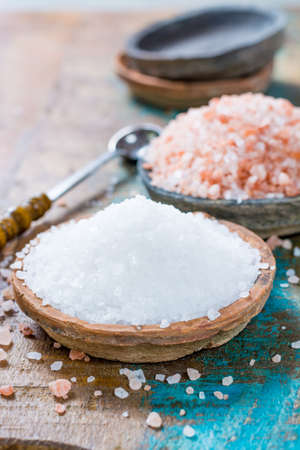 Different types of natural salt in stone bowls on wooden surface. White sea salt, pink Himalayan saltの写真素材