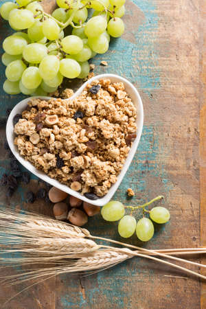 Healthy granola muesli breakfast with grape, nuts and wheat ears, love it concept, in white ceramic heart shape bowl, close upの写真素材