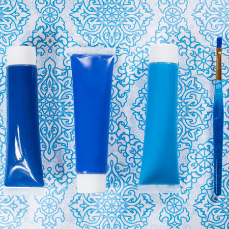 Blue, indigo, cobalt colours - home interieur design concept, on blue-white ornament, tubes with acrylic paint and blue brushの写真素材